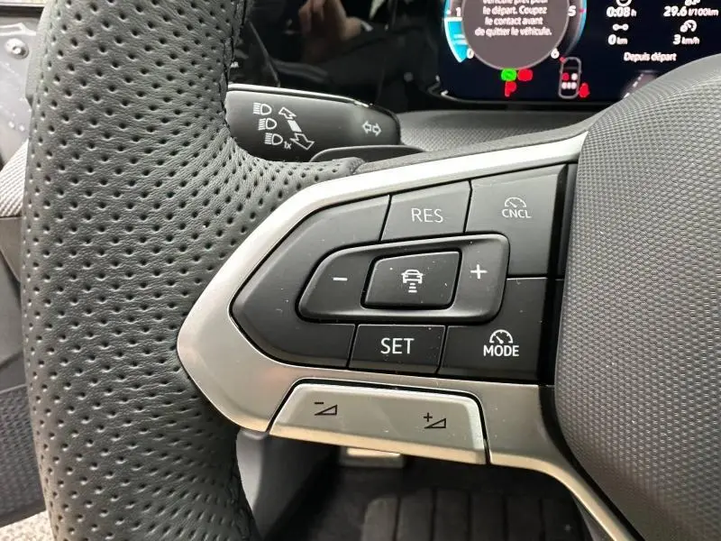 Gros plan sur les commandes de régulateur de vitesse au volant cuir perforé de la Volkswagen Golf gris Urano 2026.