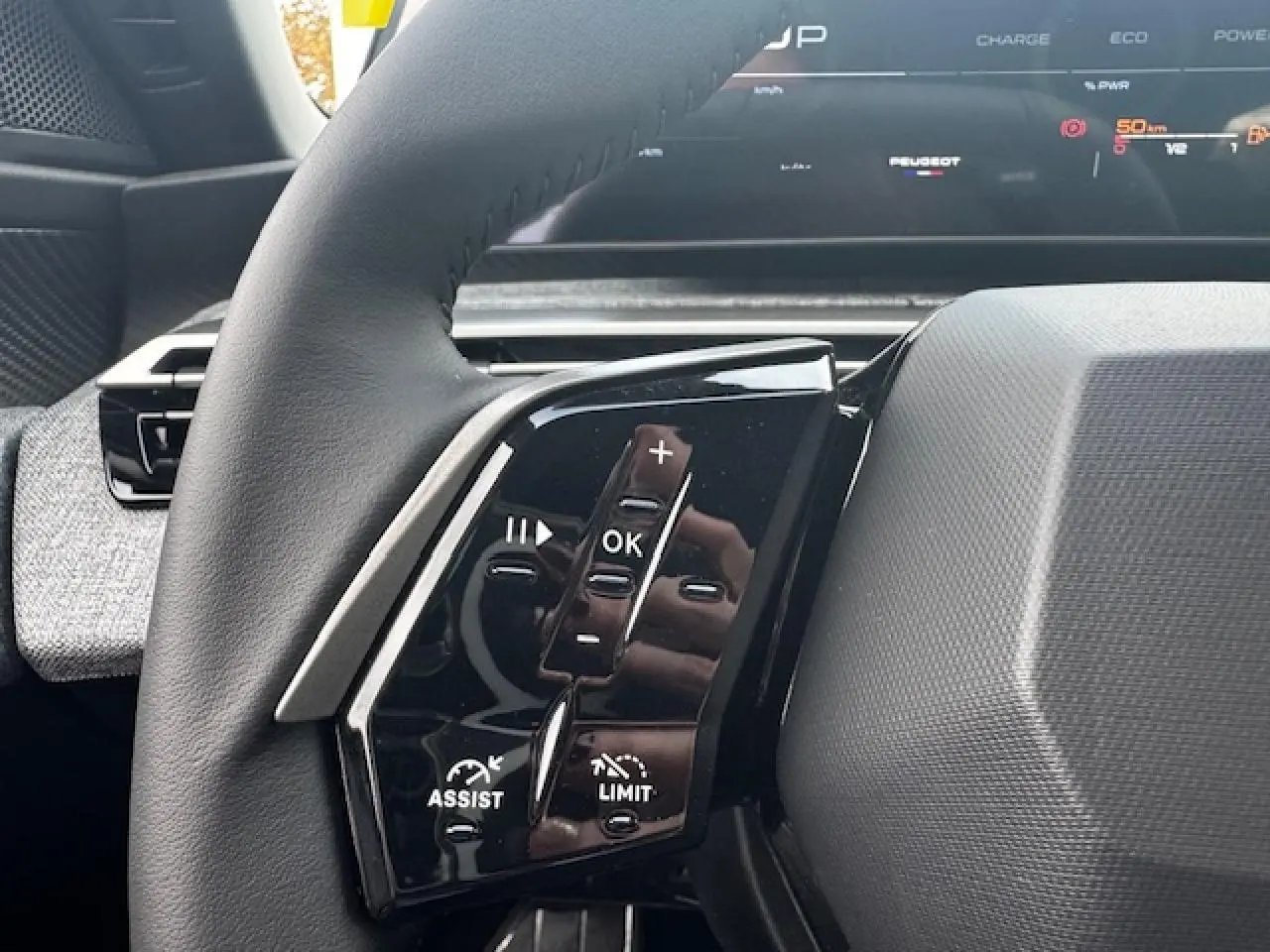 Gros plan sur les commandes gauche du volant cuir noir du Peugeot 5008 2025 avec tableau de bord numérique en arrière-plan.