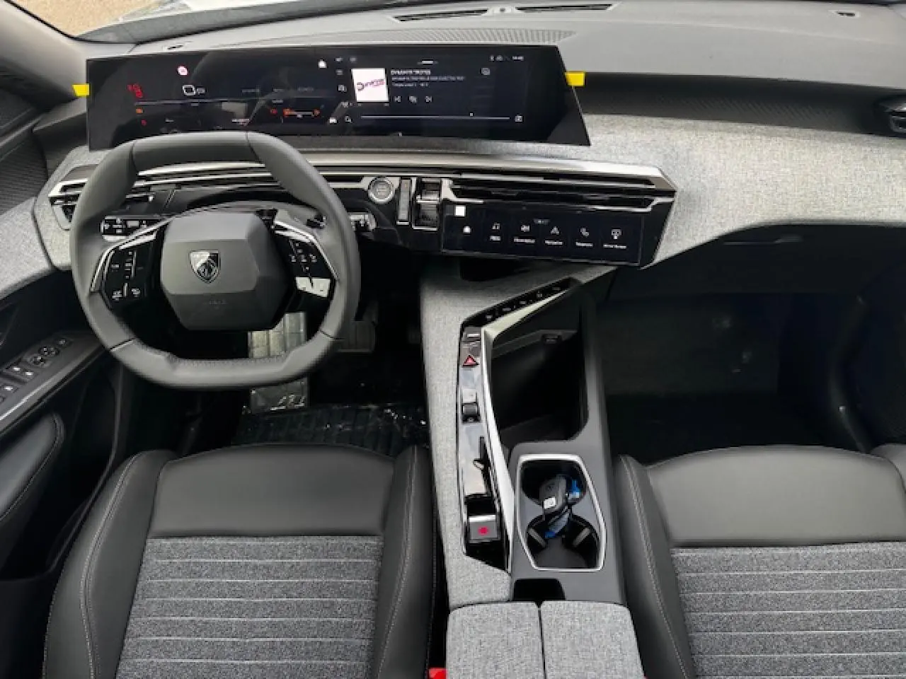 Vue intérieure avant du Peugeot 5008 2025, tableau de bord moderne avec i-Cockpit panoramique et sellerie tissu gris et cuir noir.