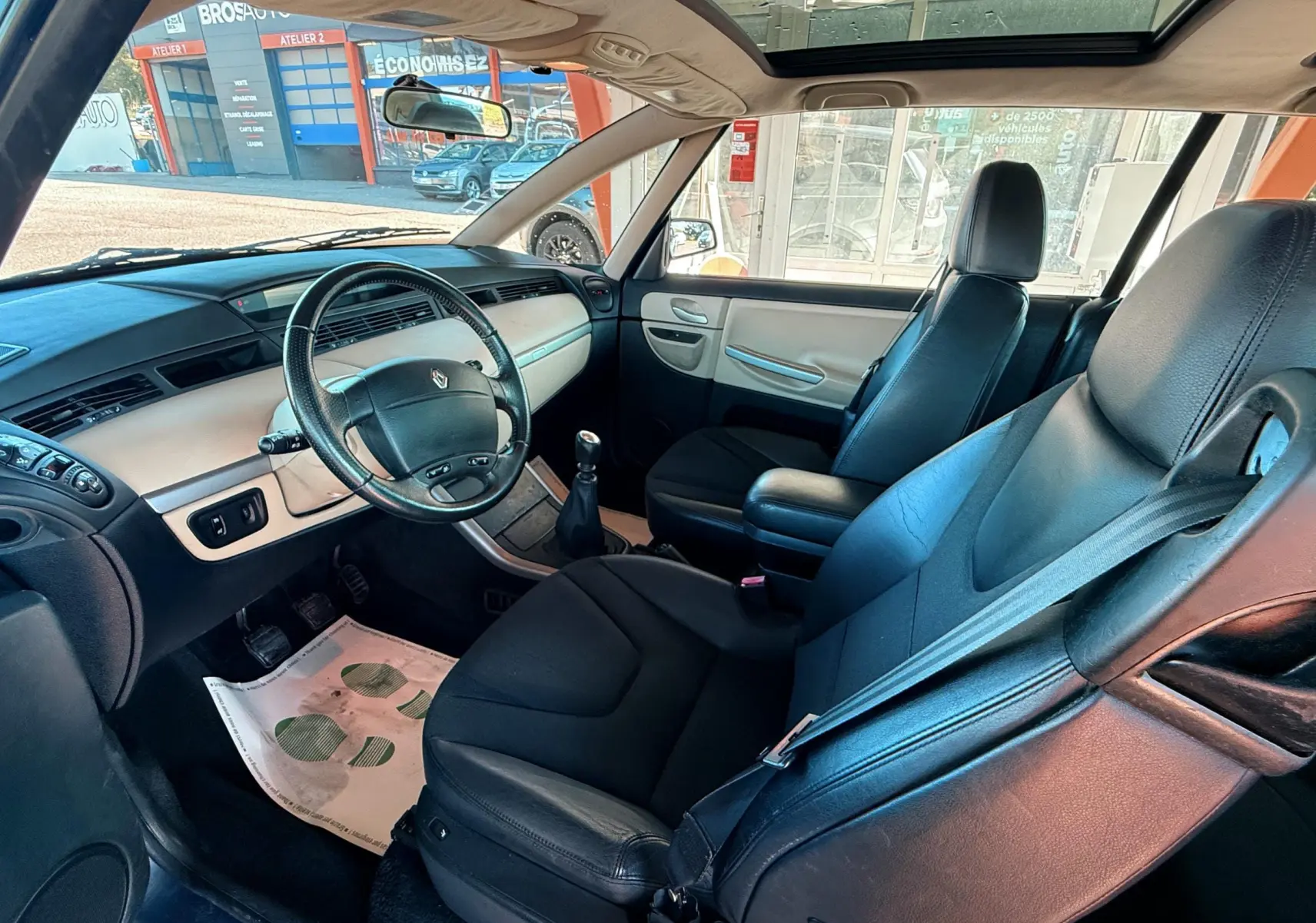 Intérieur de Renault Avantime gris, vue côté conducteur montrant sièges cuir noirs et tableau de bord clair avec toit panoramique.