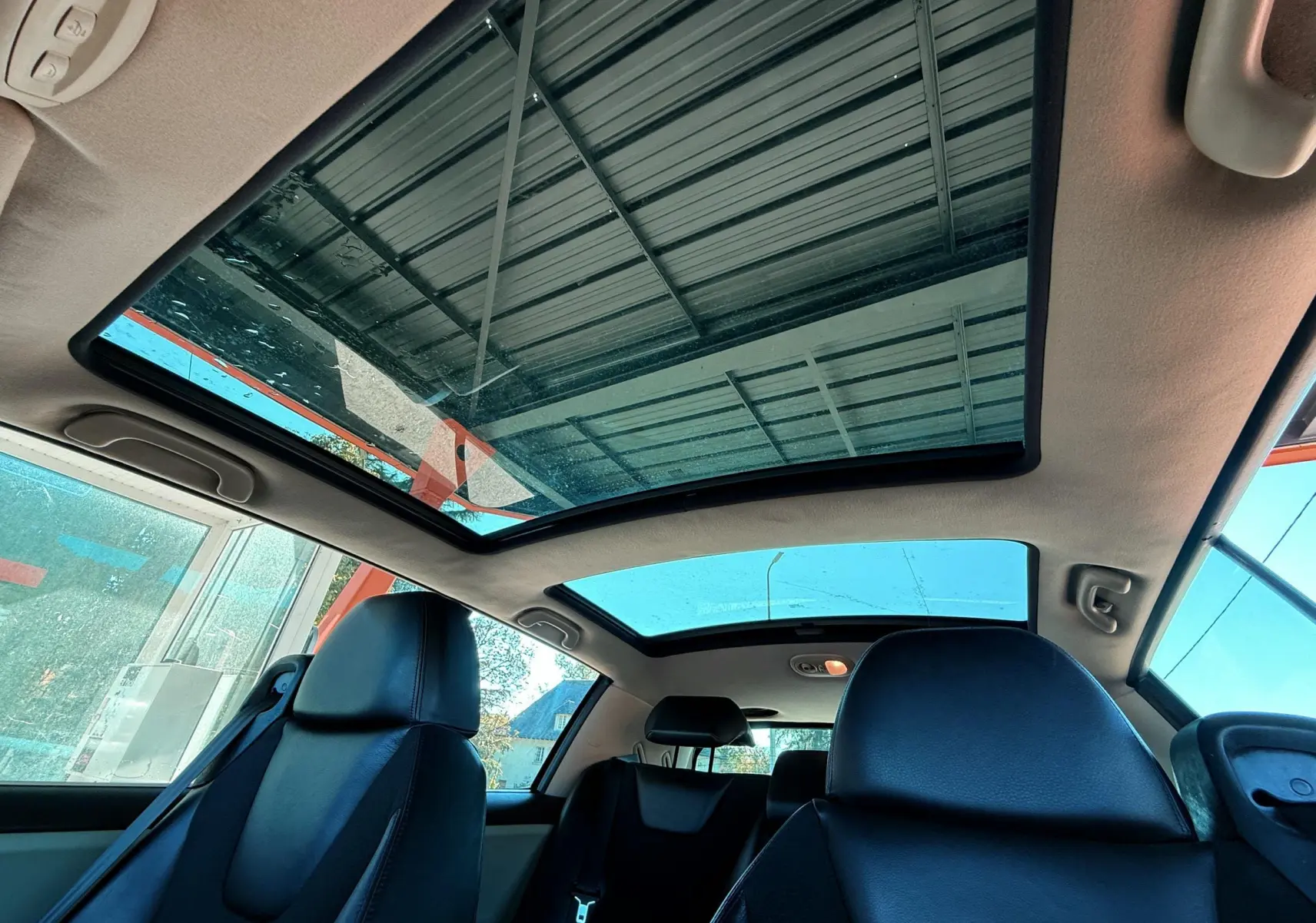 Toit panoramique en verre vu de l'intérieur arrière d'une Renault Avantime gris, sièges en cuir noir visibles.