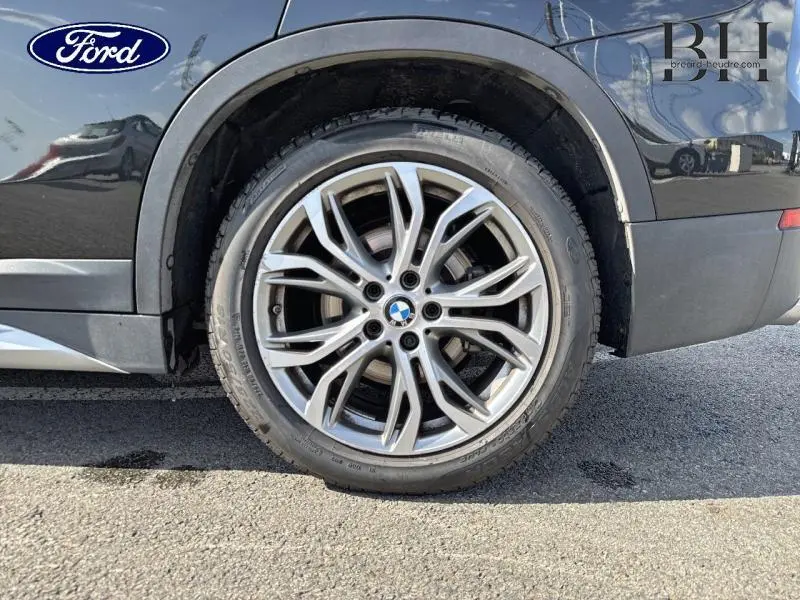 Gros plan sur la roue arrière droite d'un BMW X1 Saphirschwarz avec jante alu à rayons doubles.