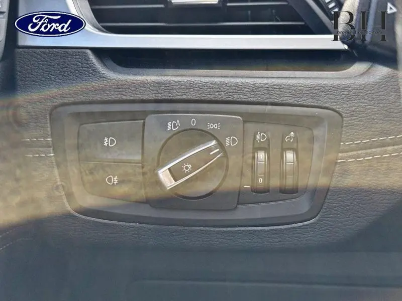 Gros plan sur le panneau de commande des phares d'un BMW X1 Saphirschwarz, avec molette et boutons rétroéclairés.