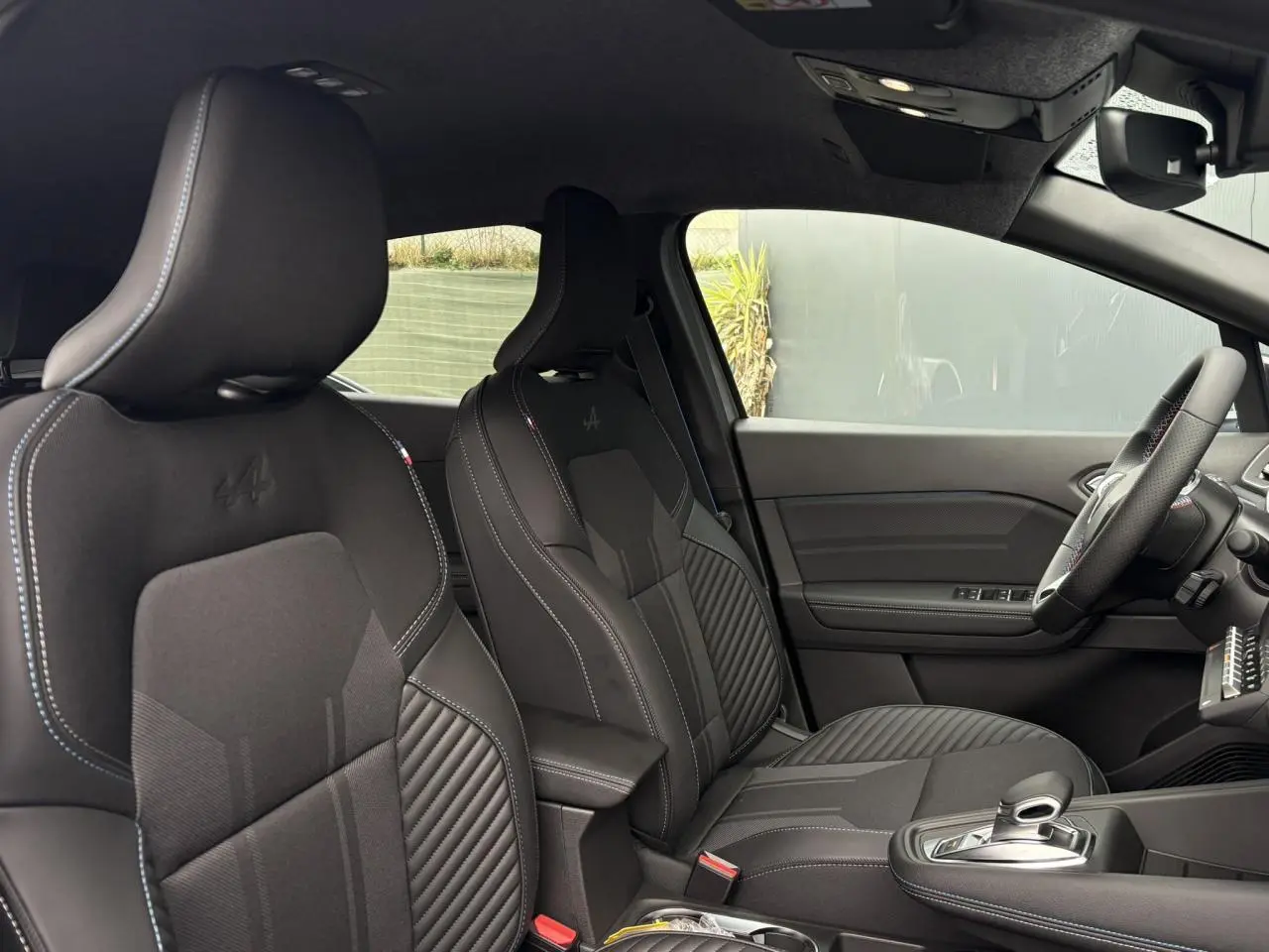 Vue intérieure côté droit du Renault Captur Esprit Alpine 2025, sièges noirs avec logo Alpine et volant surpiqué tricolore.