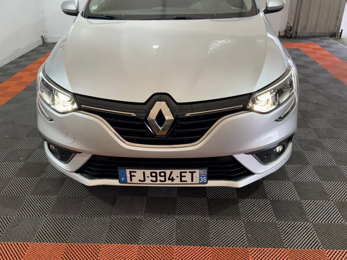 Vue avant d'une Renault Mégane gris clair avec phares allumés et calandre noire brillante.