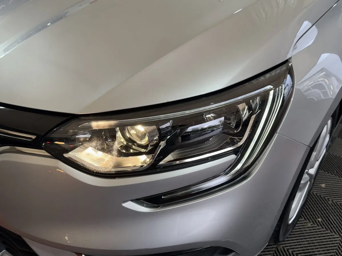 Gros plan sur le phare avant droit d’une Renault Mégane Business gris clair, mettant en valeur les LED et la carrosserie lisse.