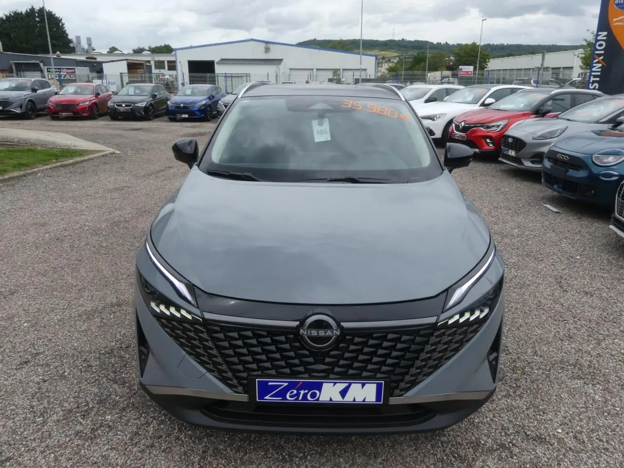 Vue avant d'un Nissan Qashqai gris métallisé avec calandre noire et feux LED distinctifs, stationné en extérieur.