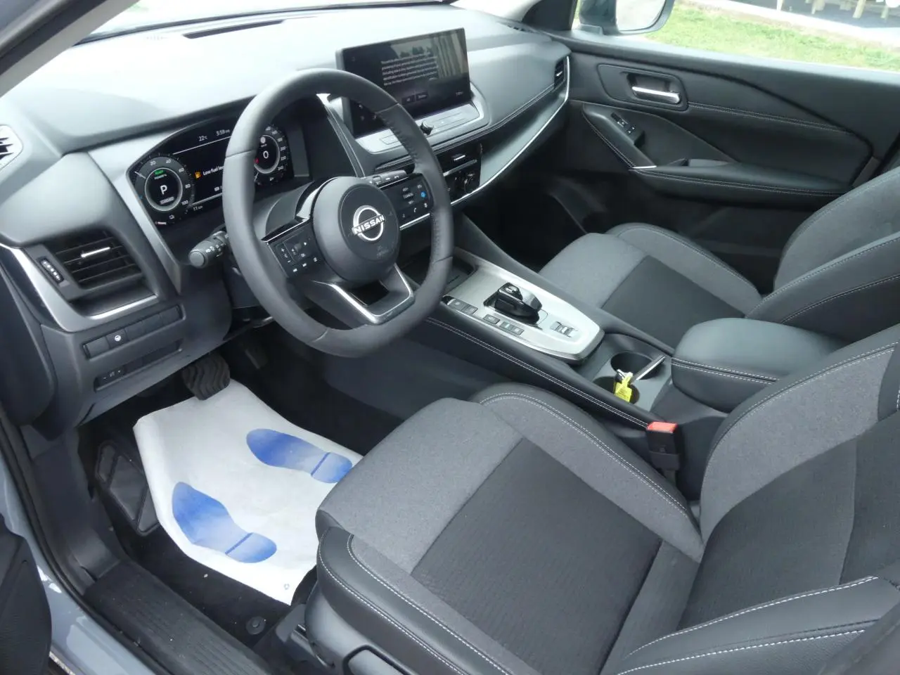 Vue intérieure côté conducteur du Nissan Qashqai 1.5 e-Power 2025 avec sellerie gris foncé et tableau de bord numérique.
