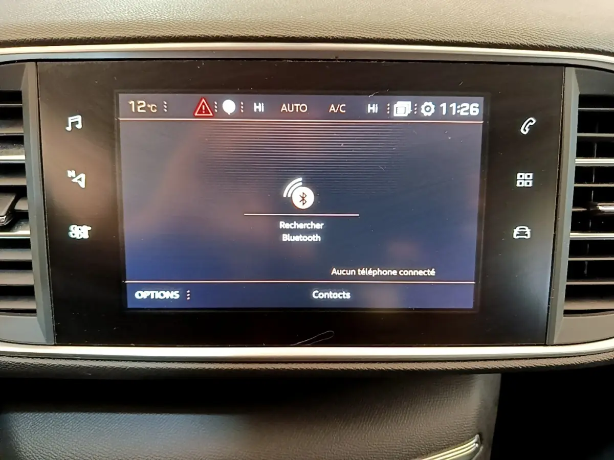 Écran tactile central de la Peugeot 308 blanc, affichant la recherche Bluetooth, entouré de commandes noires.