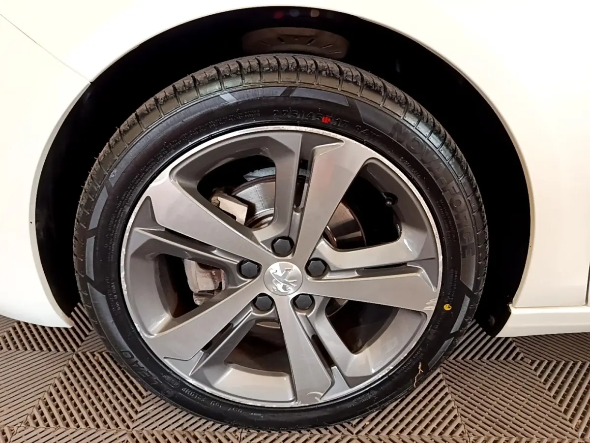 Gros plan sur la roue avant droite d'une Peugeot 308 blanche, mettant en valeur la jante alliage grise et le logo lion central.
