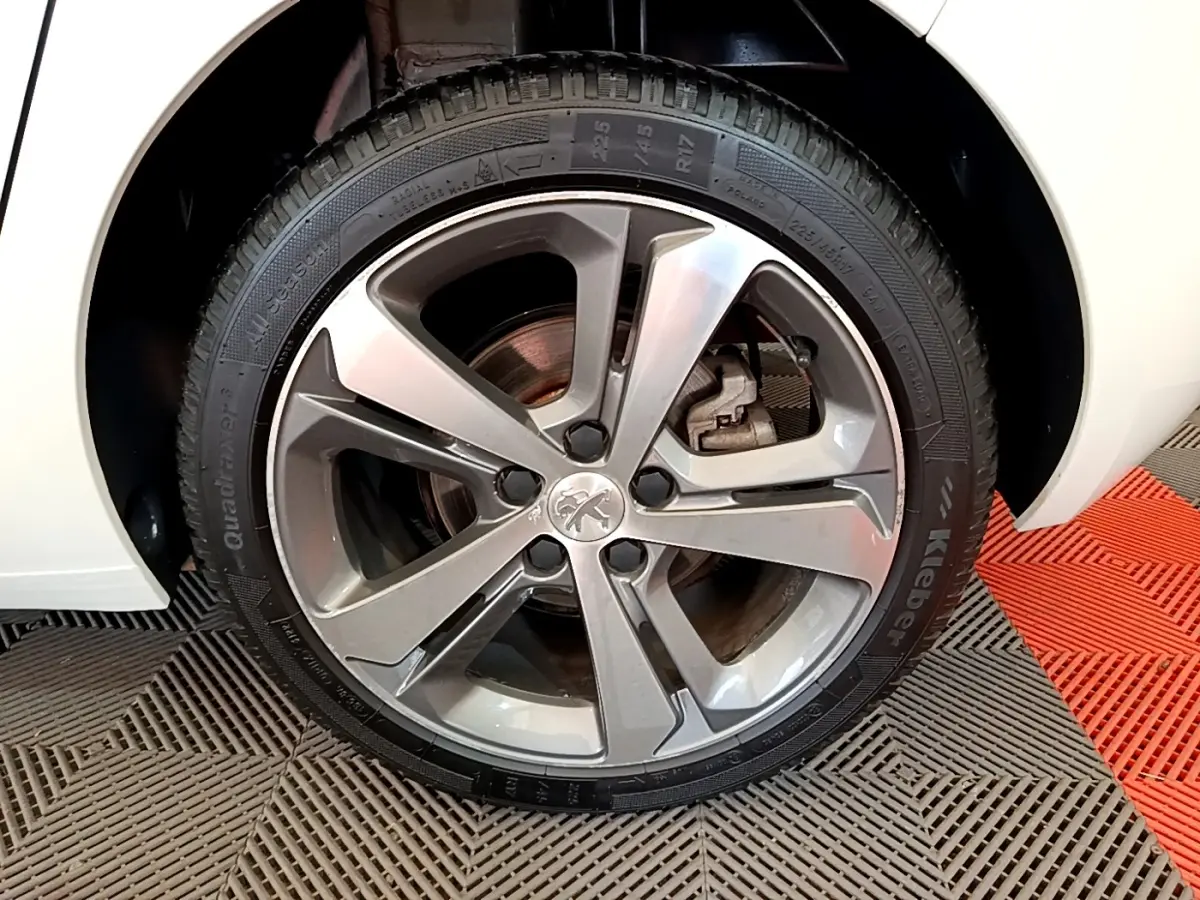 Gros plan sur la roue avant droite d'une Peugeot 308 blanche, avec jante alliage et logo lion au centre.