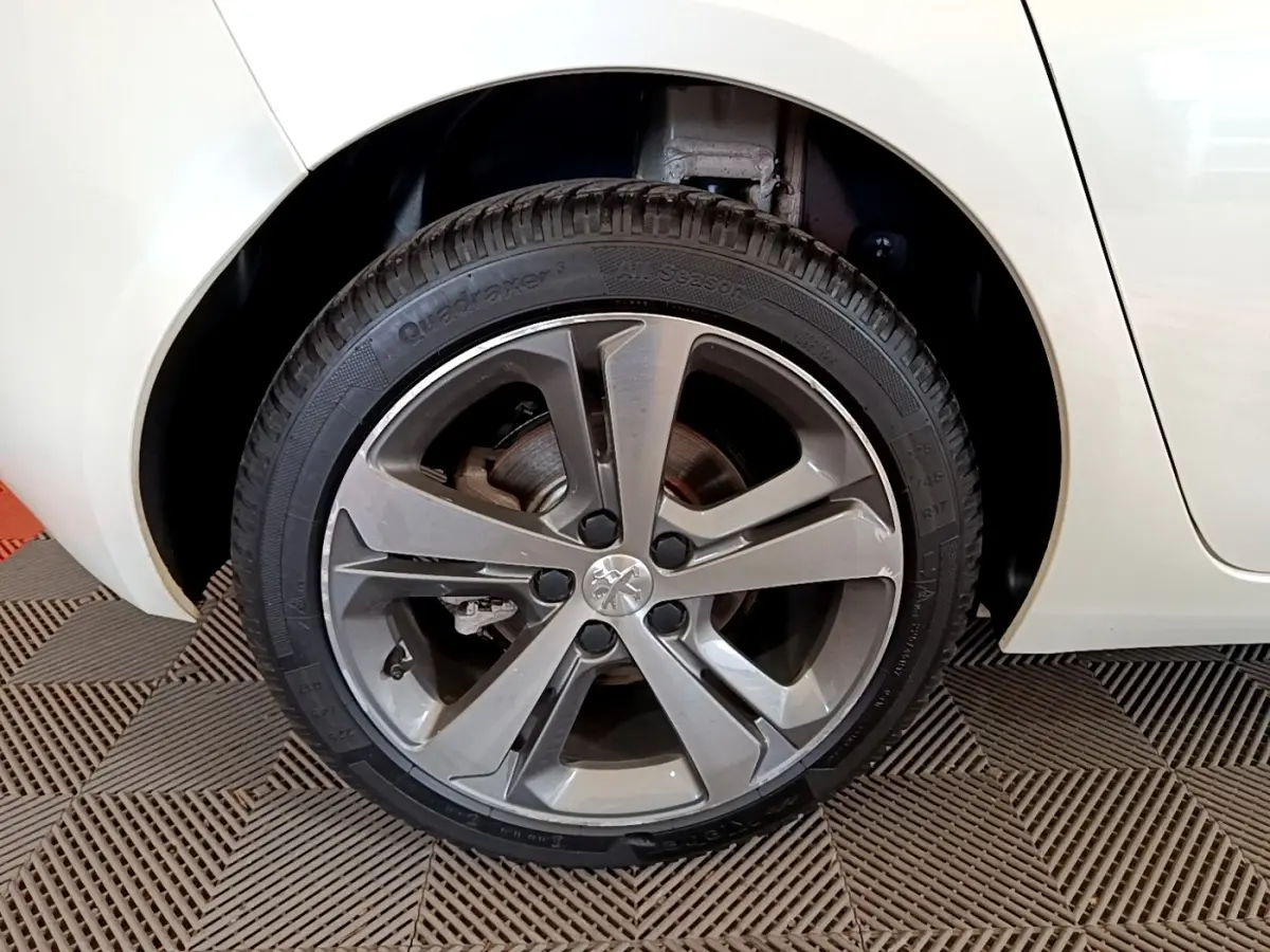 Gros plan sur la roue arrière droite d’une Peugeot 308 blanche, mettant en valeur la jante alliage grise au design moderne.