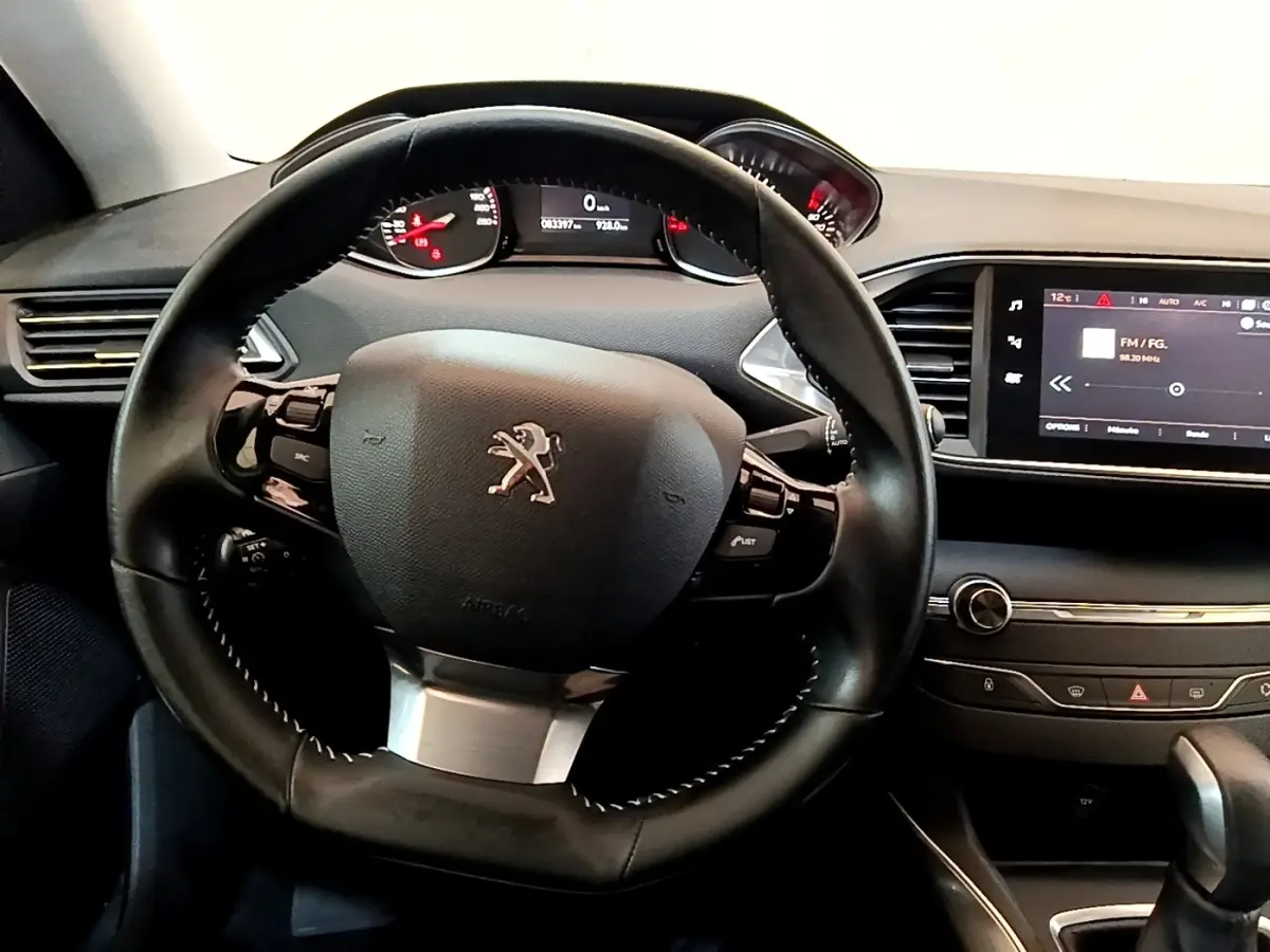 Vue intérieure centrée sur le volant cuir et le tableau de bord avec écran tactile de la Peugeot 308 blanche de 2017.