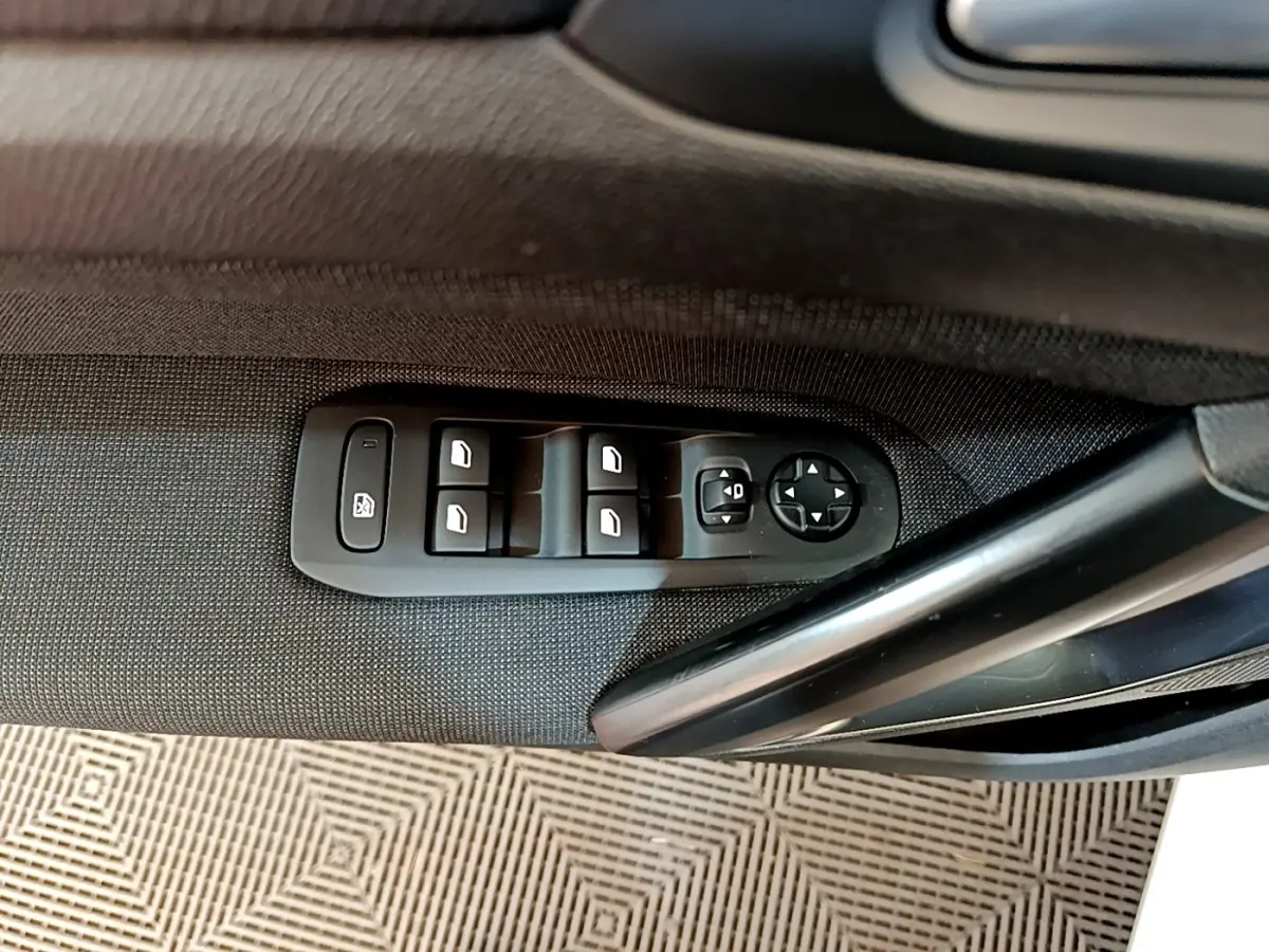 Gros plan sur les commandes des vitres et rétroviseurs côté conducteur d'une Peugeot 308 blanche de 2017.