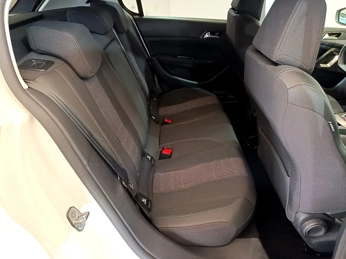 Vue intérieure côté arrière gauche de la banquette noire de la Peugeot 308 blanche, avec appuie-têtes et ceintures visibles.