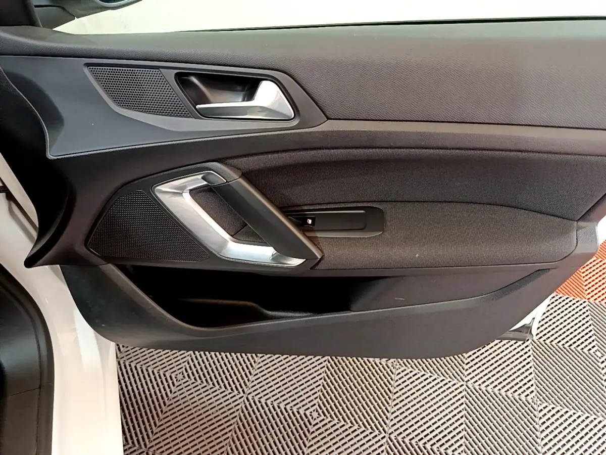 Vue rapprochée de la porte intérieure côté conducteur d’une Peugeot 308 blanche, avec poignée argentée et garniture noire.