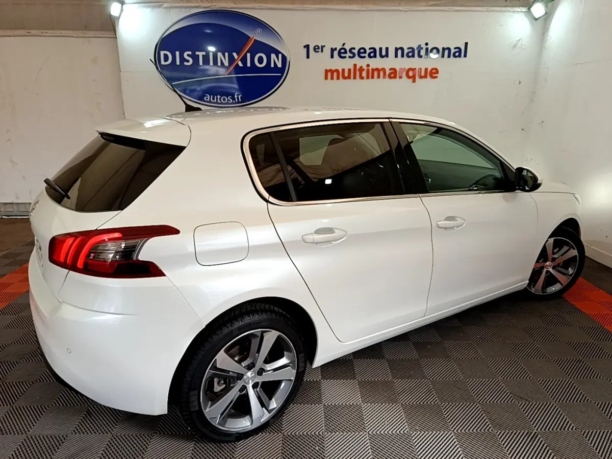 Peugeot 308 blanc vue 3/4 arrière droit, feux arrière LED et jantes alliage visibles en intérieur showroom.