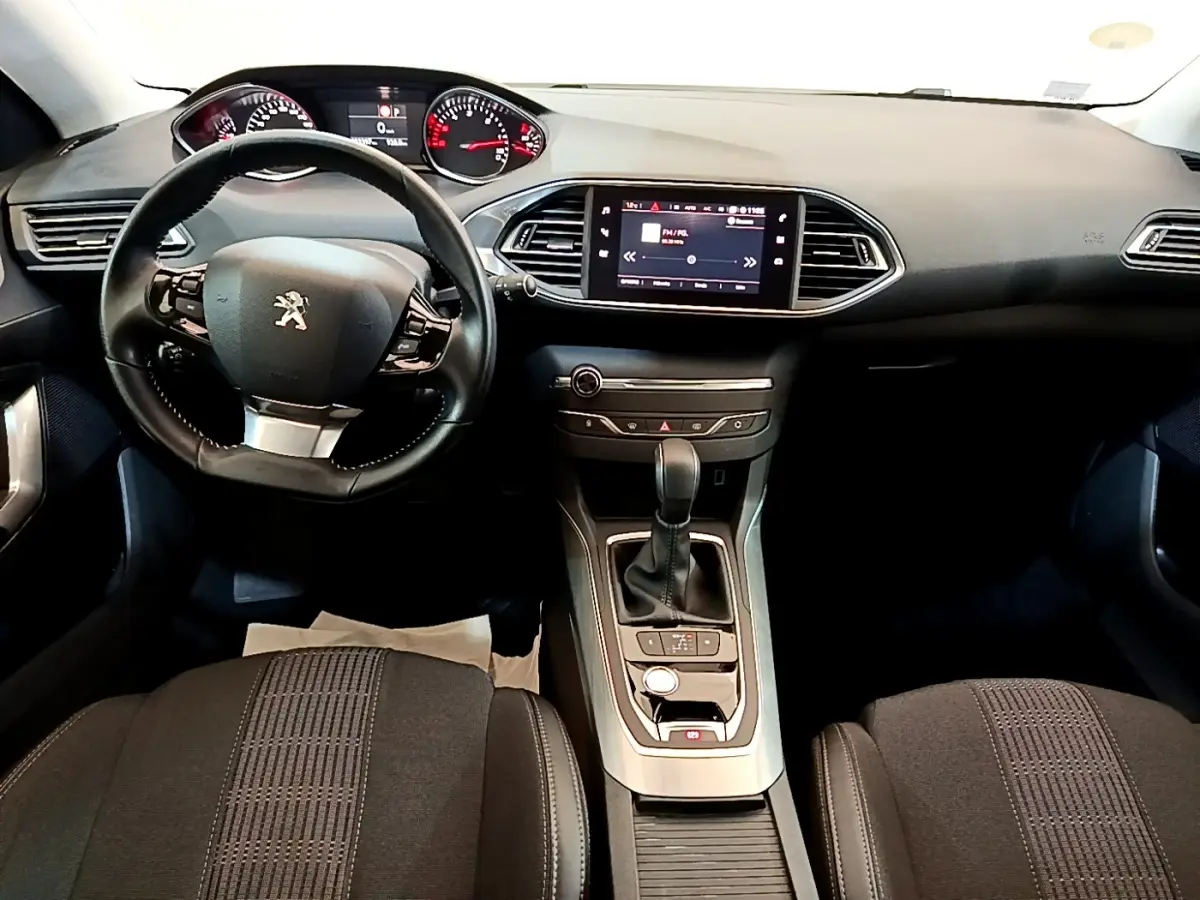 Vue intérieure avant de la Peugeot 308 2017, tableau de bord noir avec écran tactile central et volant cuir multifonctions.