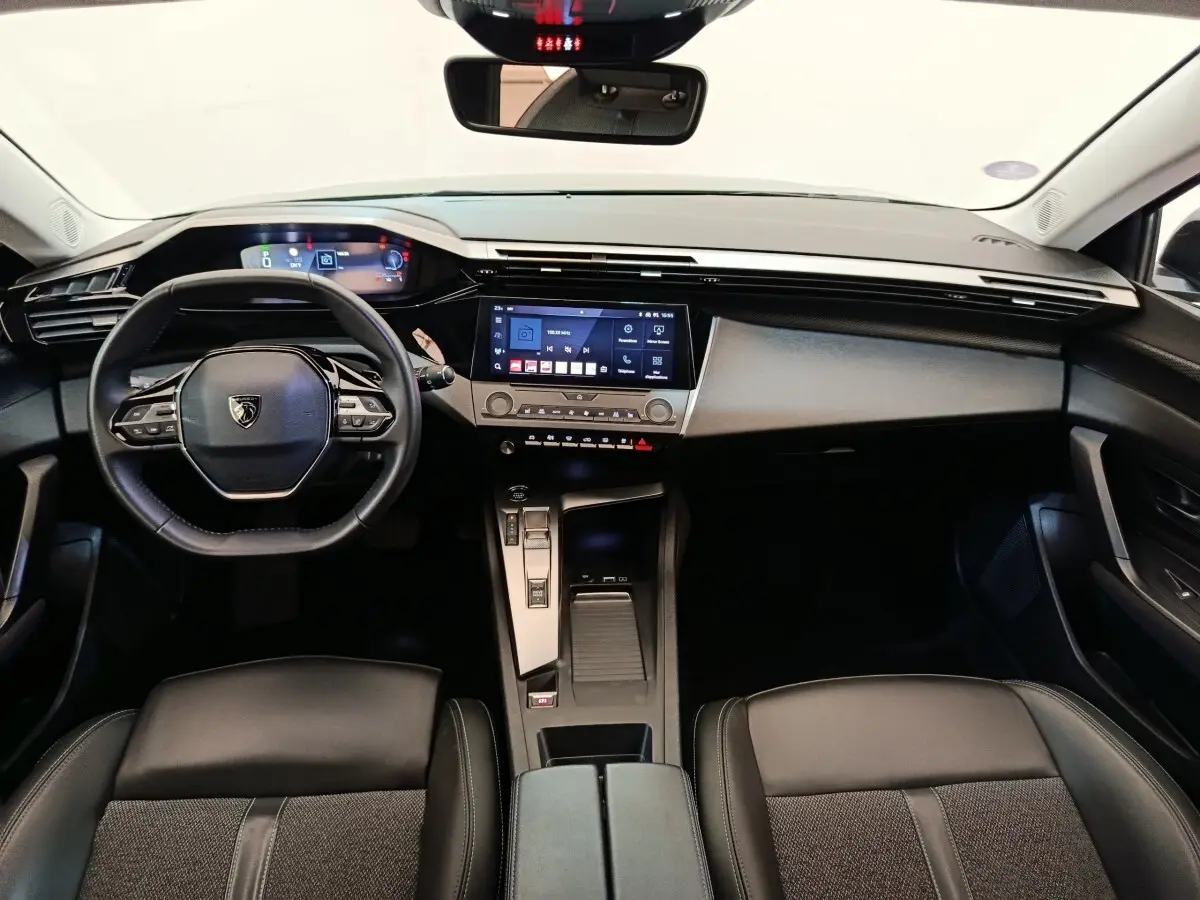 Vue intérieure avant de la Peugeot 308 2023, tableau de bord noir avec écran tactile central et volant cuir multifonctions.
