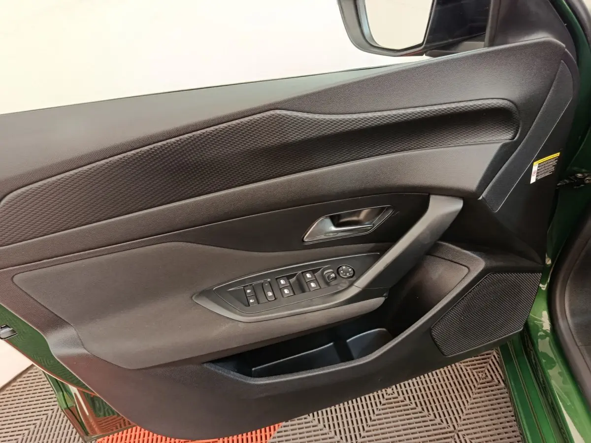 Vue intérieure côté gauche de la porte avant verte d'une Peugeot 308 avec commandes des vitres et haut-parleur intégré.