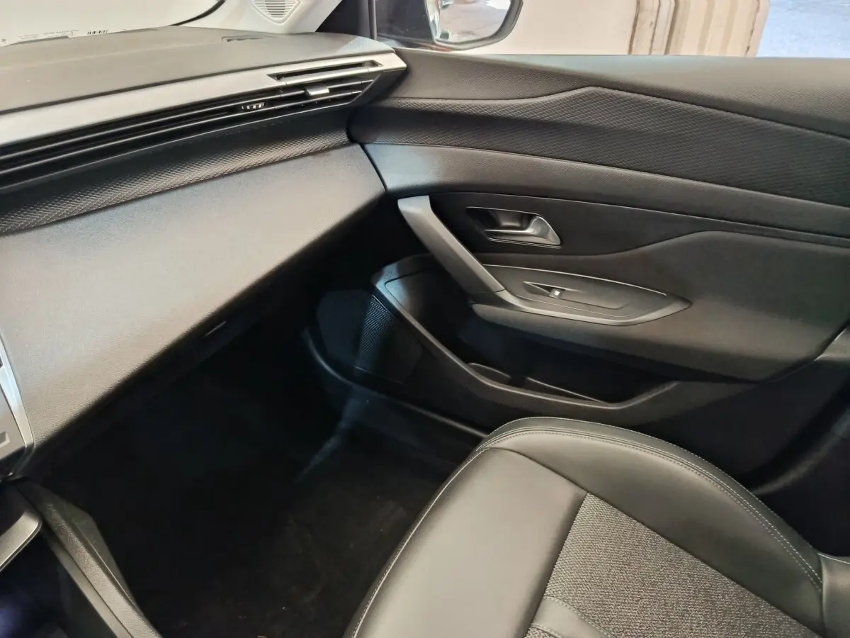 Vue intérieure côté passager de la Peugeot 308 2023, avec tableau de bord et porte en noir texturé.