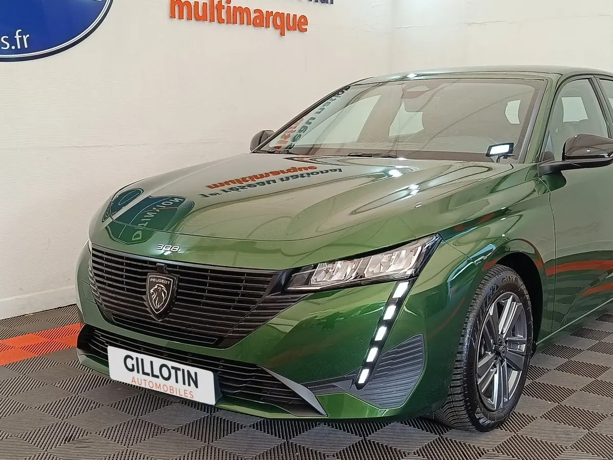 Vue 3/4 avant d'une Peugeot 308 2023 vert métallisé avec feux LED verticaux et calandre noire distinctive.