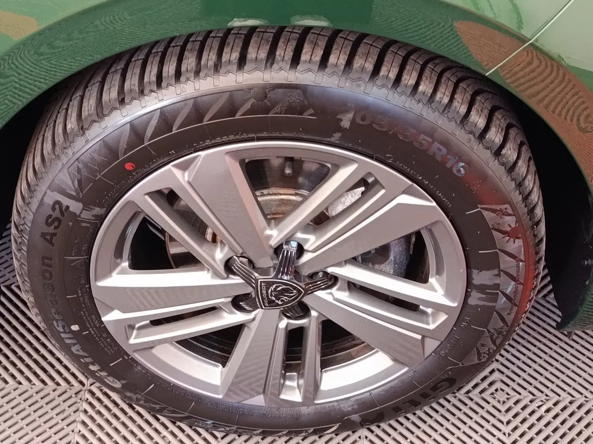 Gros plan sur la roue avant droite d'une Peugeot 308 vert 2023 avec jante alliage et logo Peugeot central.