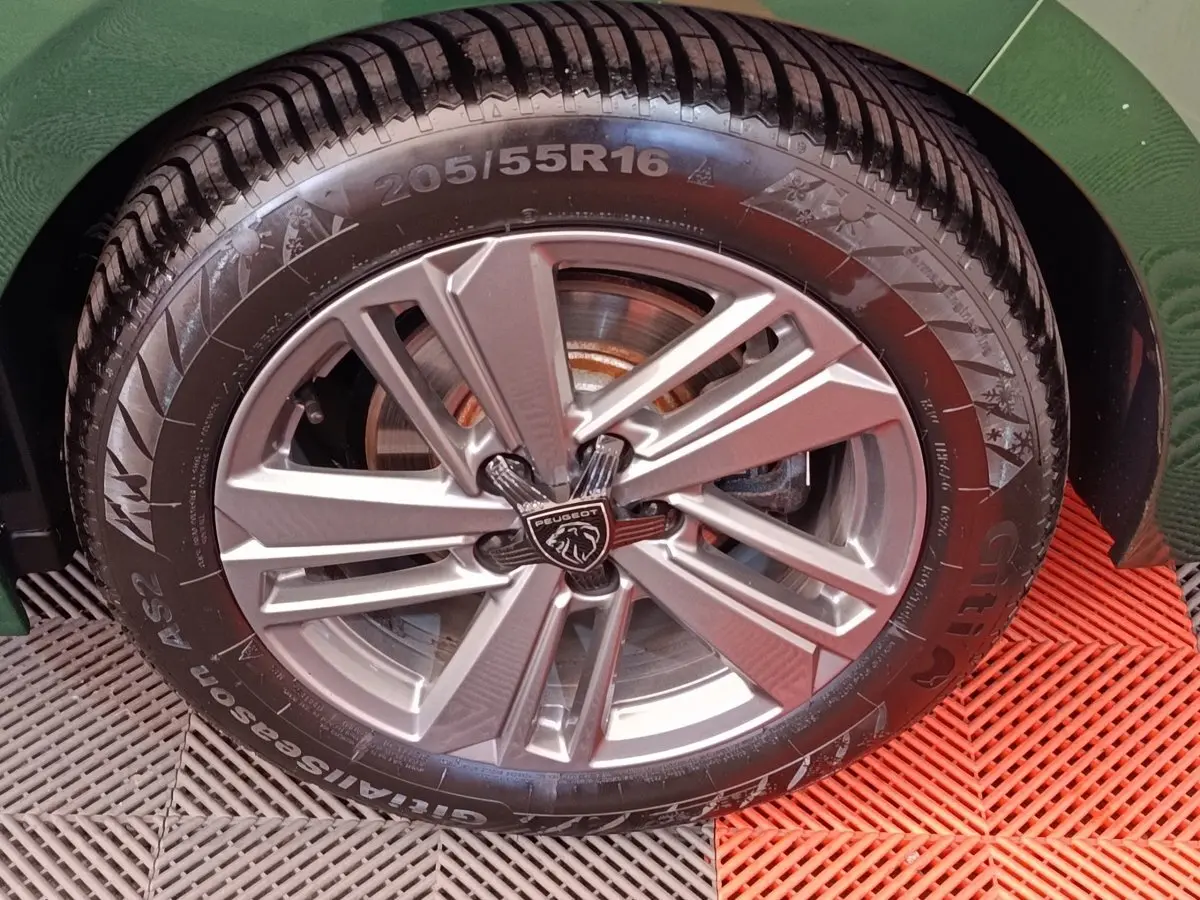 Gros plan sur la roue avant droite d'une Peugeot 308 vert 2023 avec jante alliage et logo lion central.