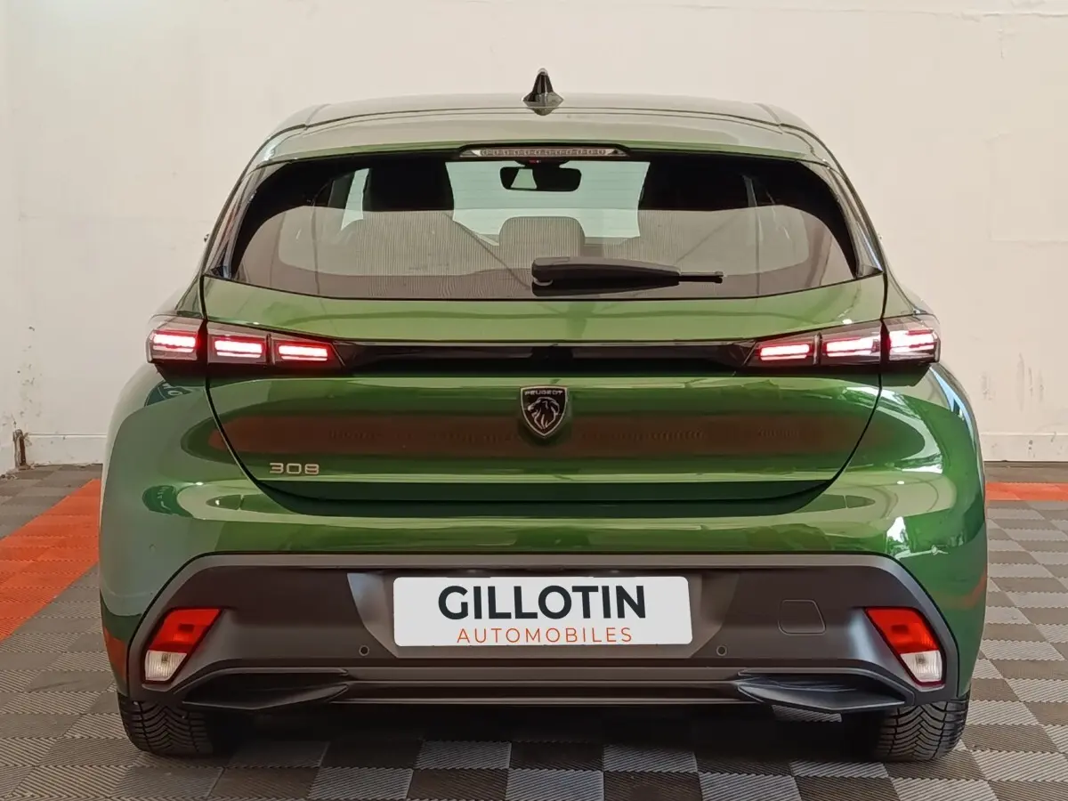 Vue arrière d’une Peugeot 308 2023 vert métallisé avec feux LED allumés et logo lion central sur hayon.