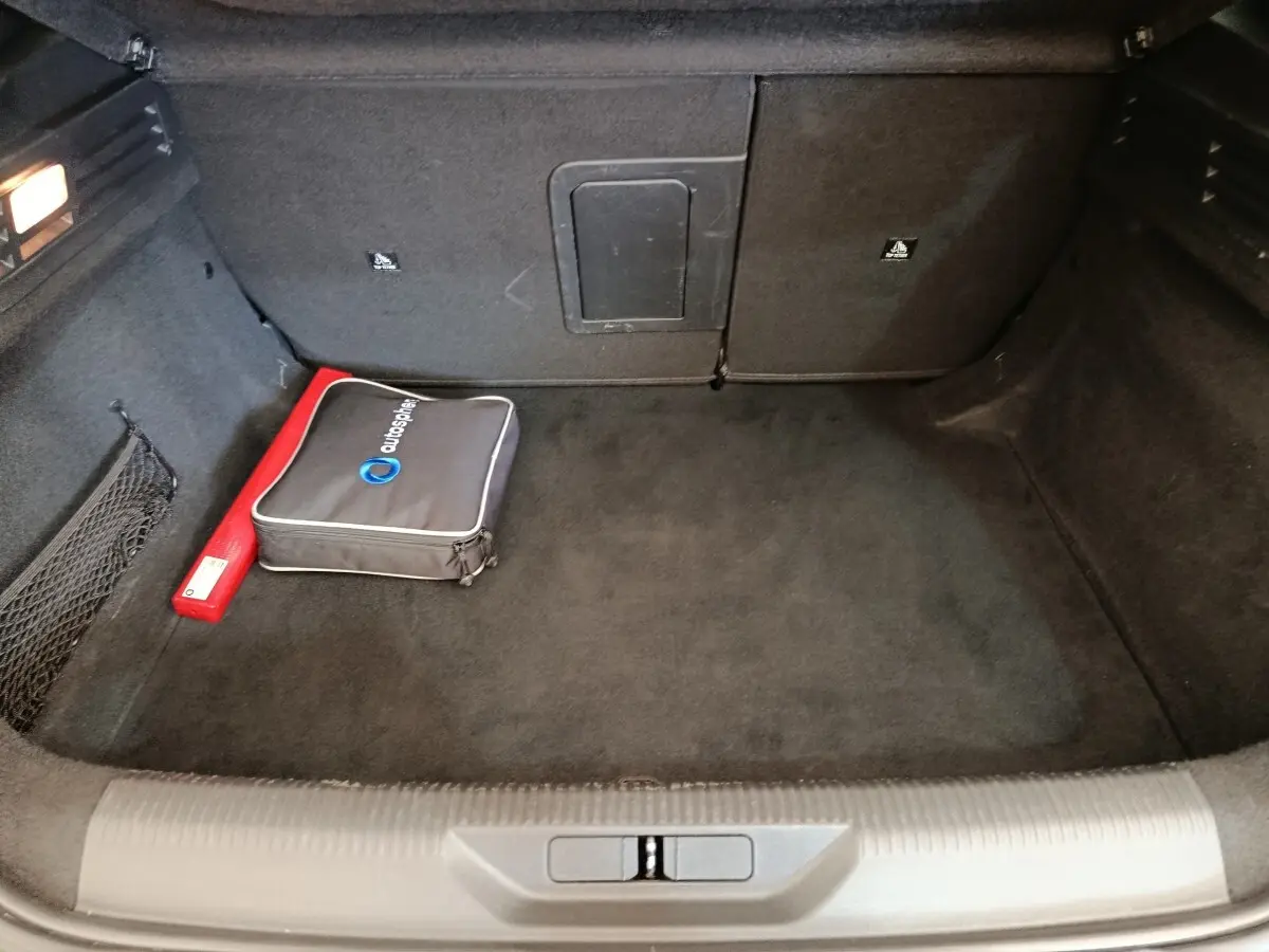 Coffre ouvert de la Peugeot 308 vert, vue intérieure montrant un rangement noir avec trousse et triangle de sécurité.