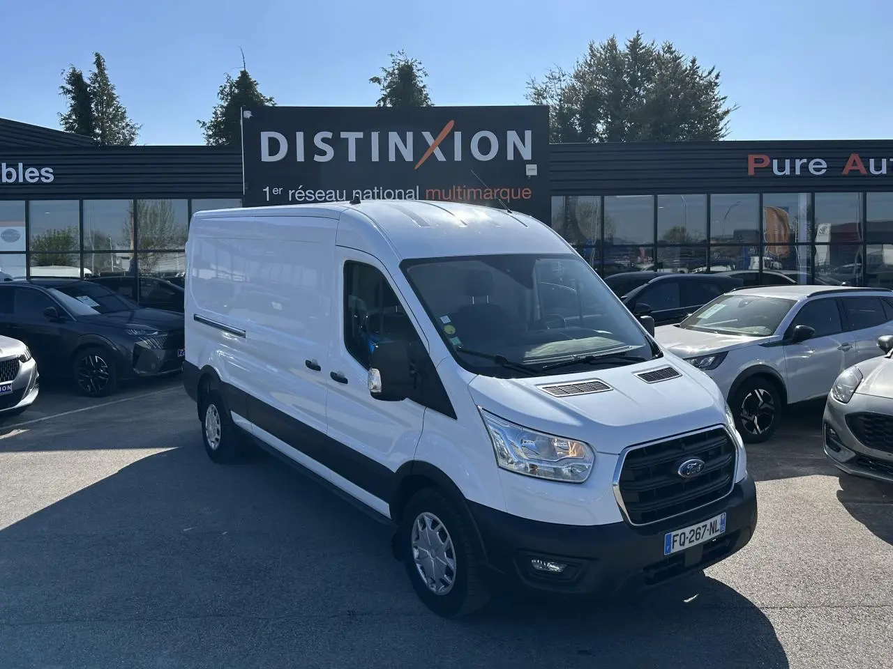 Ford Transit Fourgon blanc vu en 3/4 avant droit sur un parking devant un bâtiment commercial.