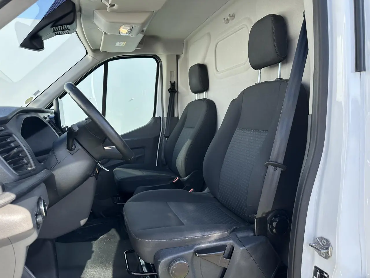 Vue intérieure côté conducteur du Ford Transit Fourgon blanc 2020, montrant les sièges noirs et le volant.