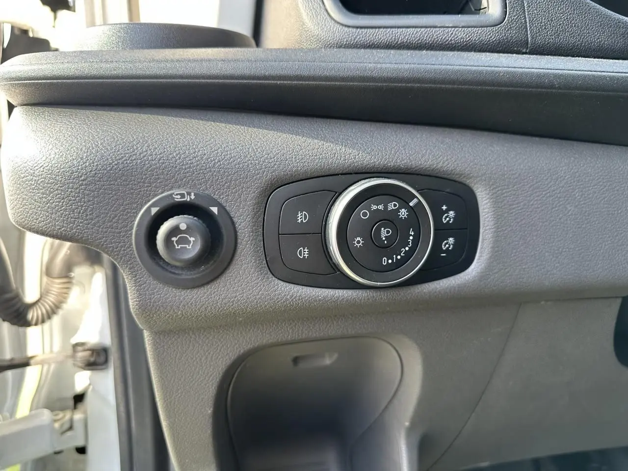 Gros plan sur les commandes d'éclairage et de réglage des rétroviseurs du Ford Transit Fourgon blanc, côté conducteur.