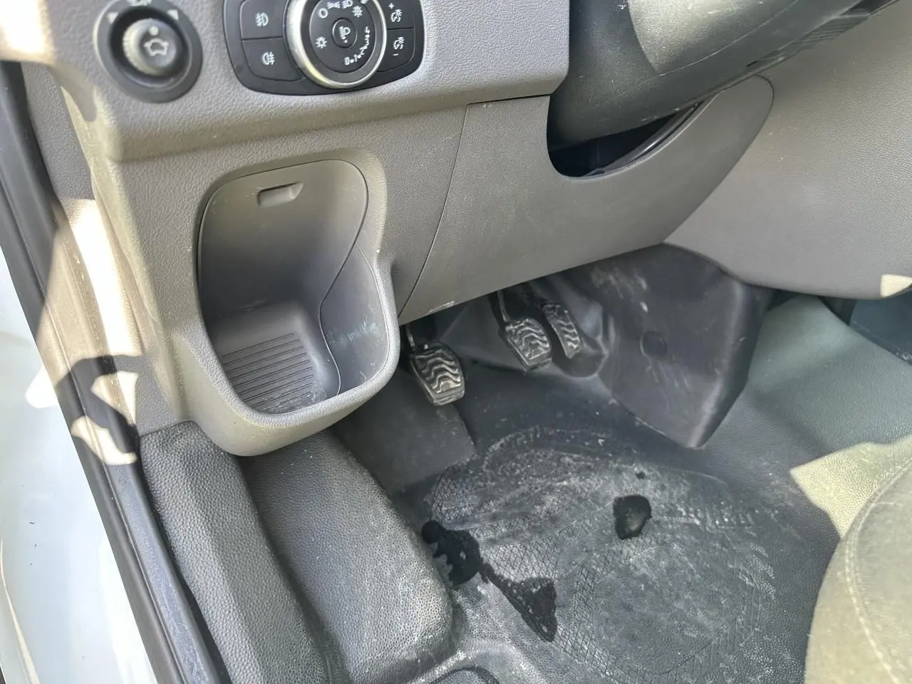 Vue rapprochée côté conducteur du pédalier et du rangement sous tableau de bord du Ford Transit Fourgon blanc 2020.