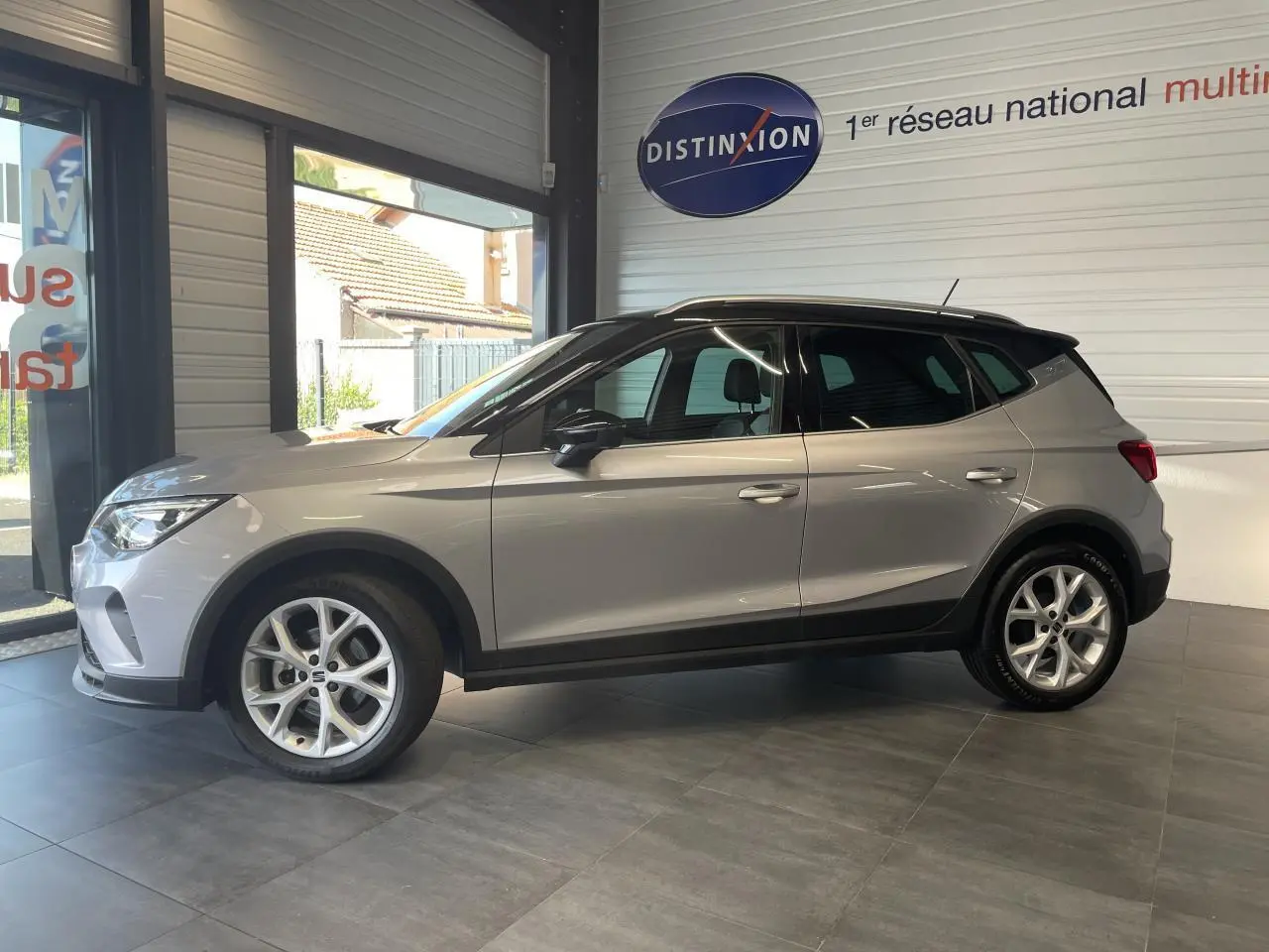 Vue de profil côté gauche d'un SEAT Arona 2024 gris GRS avec jantes alliage et toit noir en showroom.