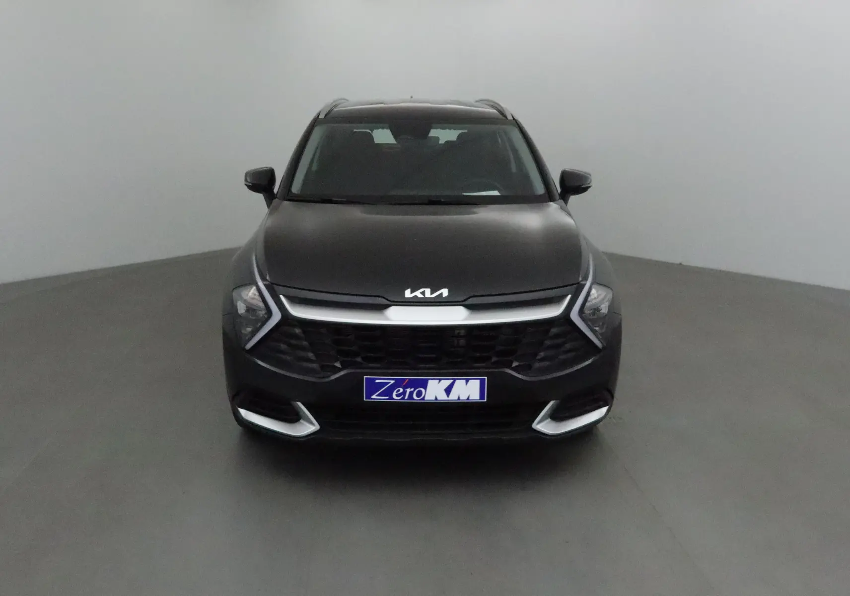 Vue frontale d'un KIA Sportage noir 2025 avec calandre large et éclairage LED en forme de flèche.