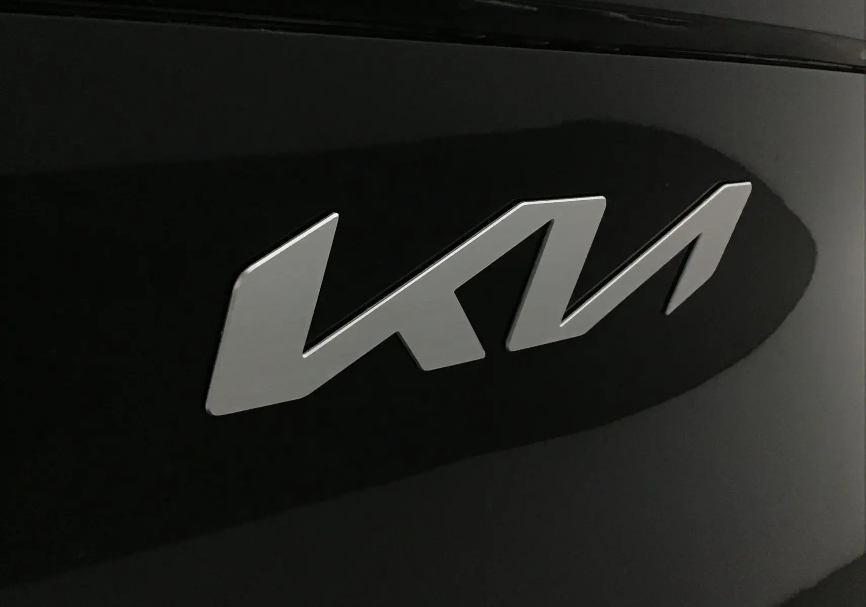Gros plan sur le logo KIA argenté sur la carrosserie noire brillante du SUV Sportage 2025.