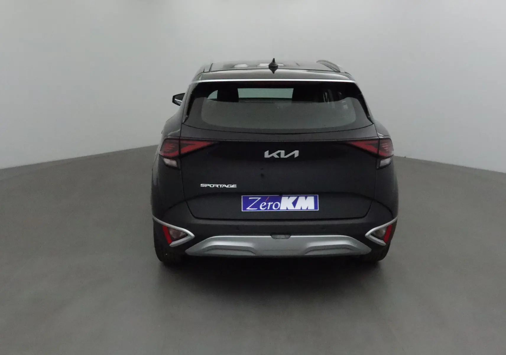 Vue arrière du KIA Sportage noir 2025 avec feux LED et logo distinctif sur fond neutre.
