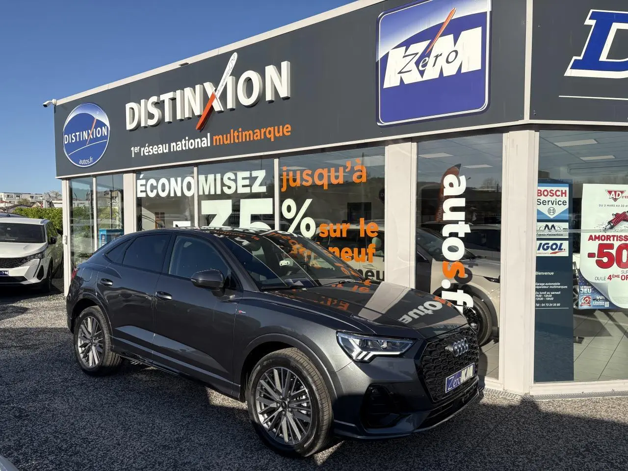 Audi Q3 Sportback gris Daytona vue 3/4 avant droit avec jantes 20 branches et calandre noire devant un showroom