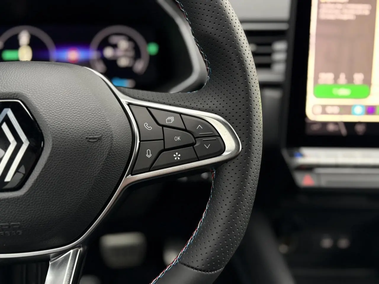 Gros plan sur le volant perforé du Renault Captur blanc nacré 2025 avec commandes intégrées et surpiqûres tricolores.