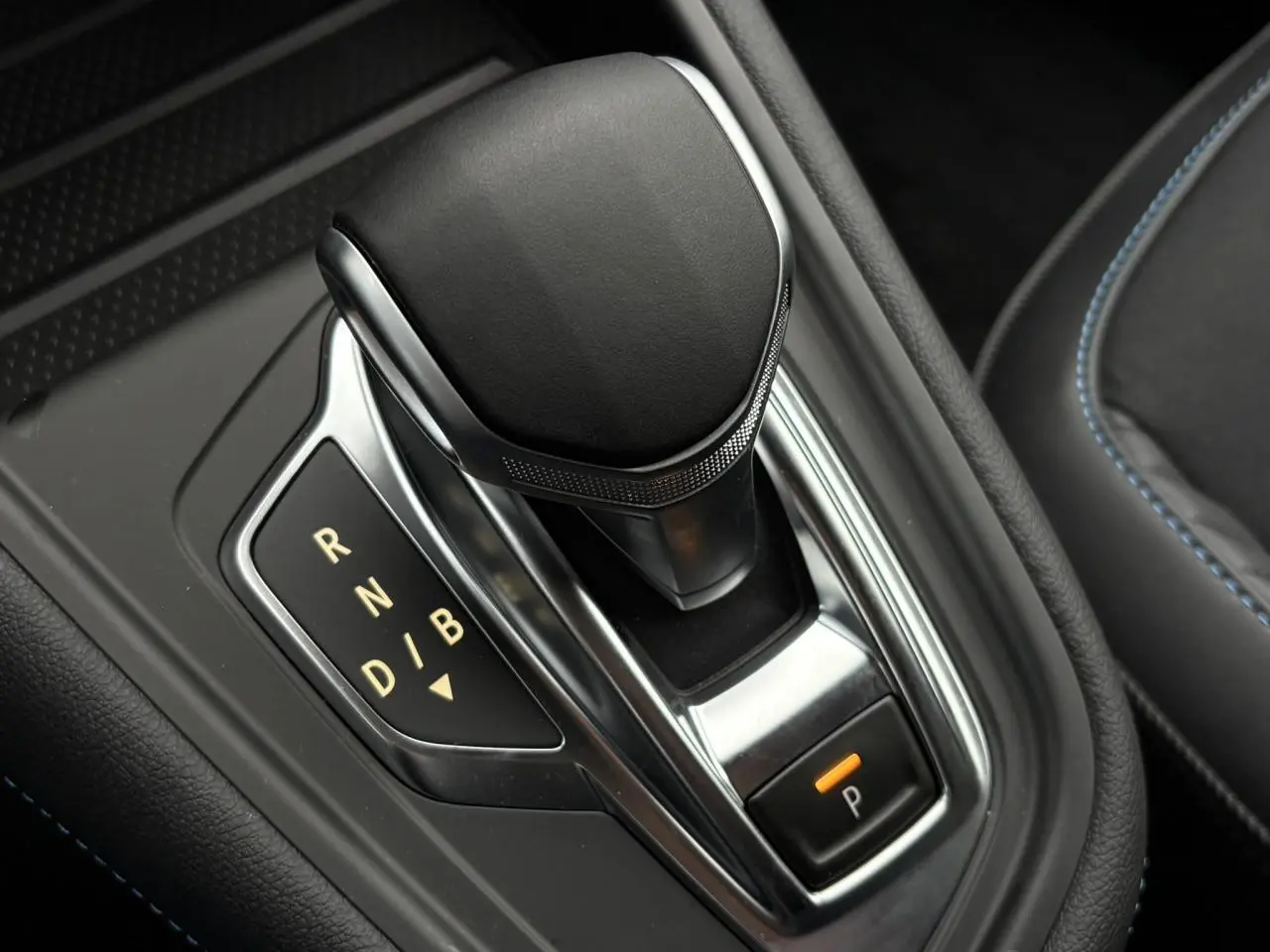 Gros plan sur le levier de vitesses noir et chrome de la Renault Captur hybride, avec surpiqûres bleues visibles sur la sellerie.