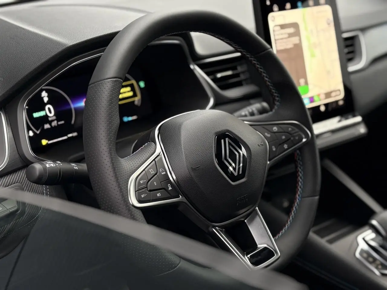 Vue rapprochée du volant noir avec logo Renault et surpiqûres tricolores, tableau de bord numérique et écran tactile visibles.