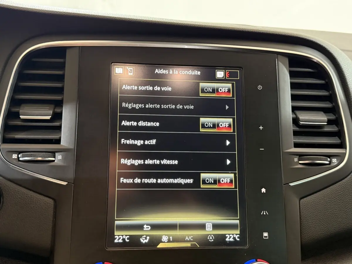 Écran tactile central de la Renault Mégane Intens gris foncé, affichant les aides à la conduite, entouré de grilles d’aération.