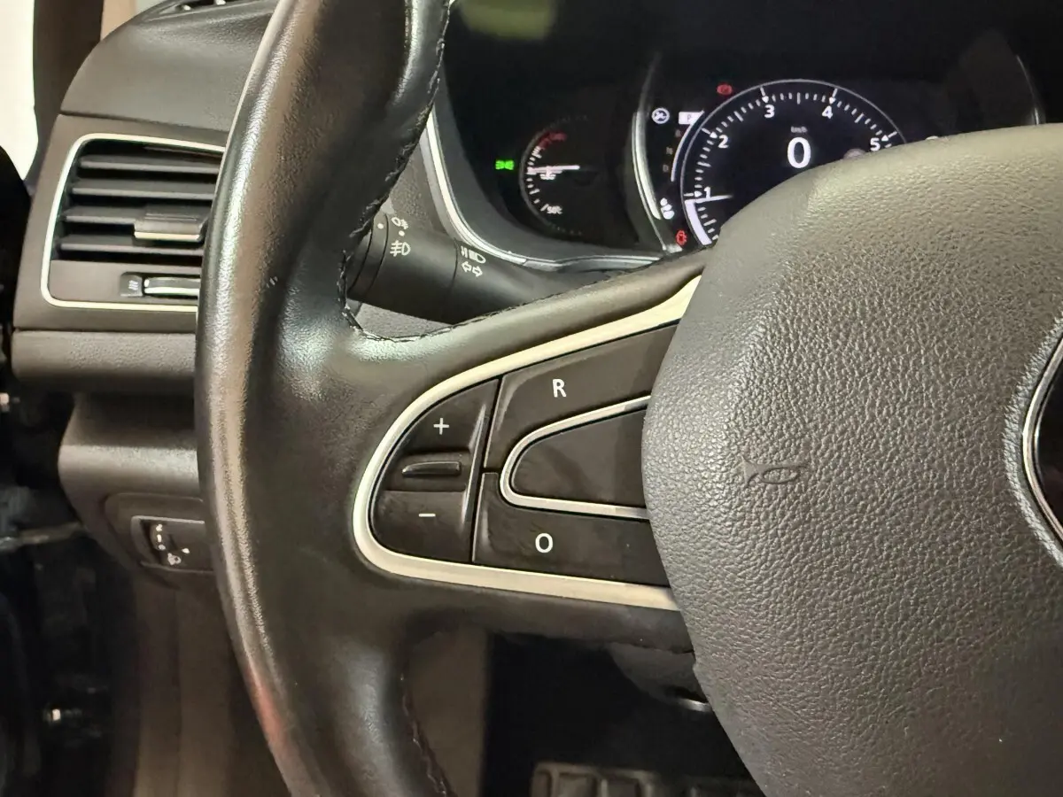 Gros plan sur le volant cuir noir de la Renault Mégane Intens, avec commandes intégrées et tableau de bord numérique en arrière-plan.