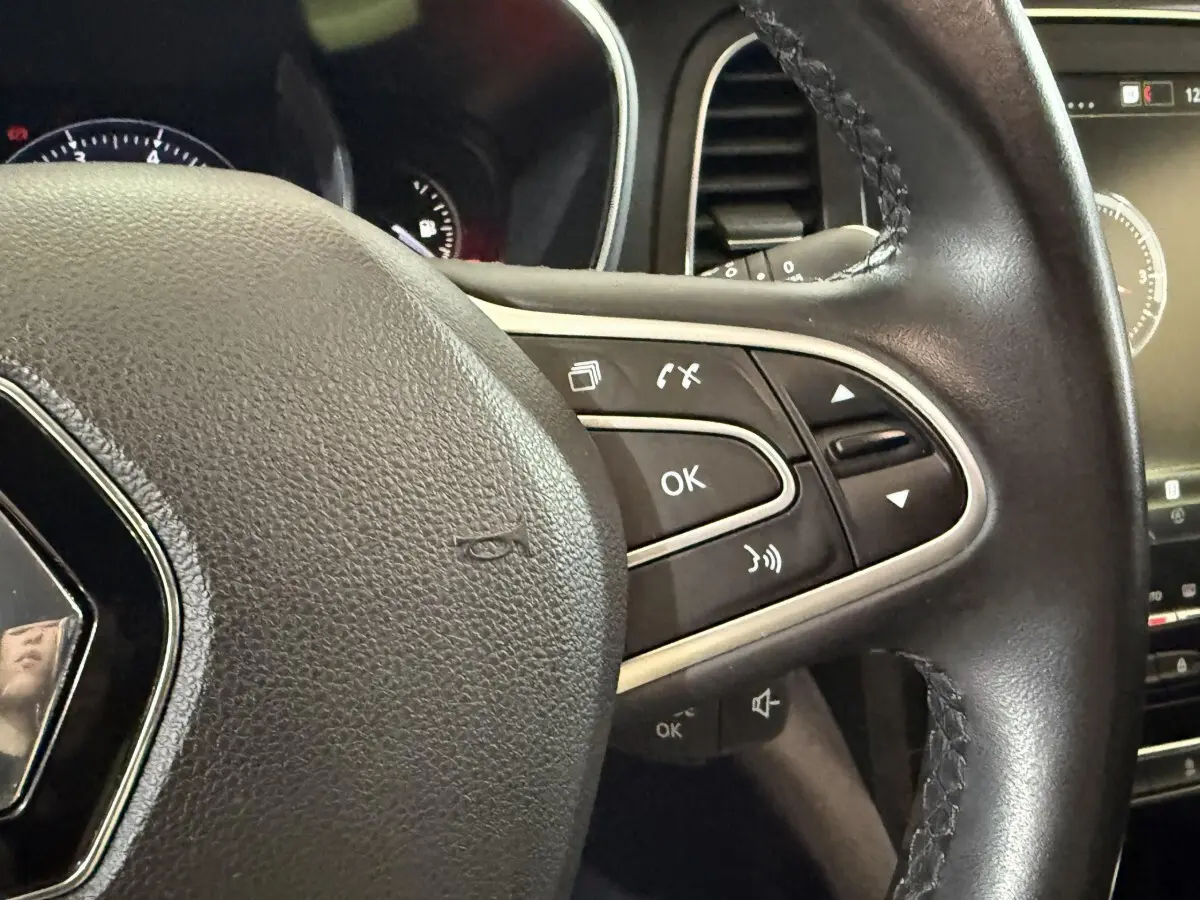 Gros plan sur le volant cuir multifonctions de la Renault Mégane Intens gris foncé avec commandes intégrées.