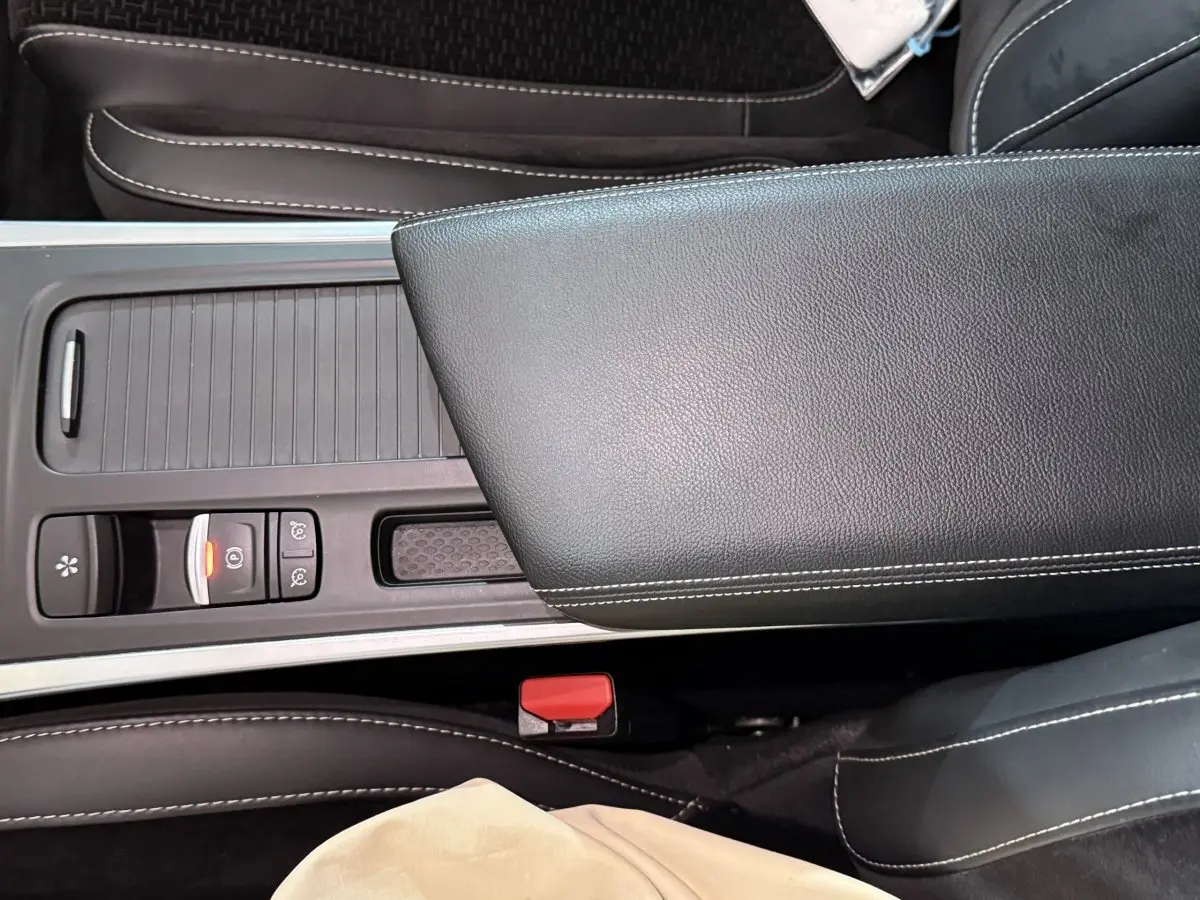 Gros plan sur la console centrale et l'accoudoir en cuir noir avec surpiqûres blanches d'une Renault Mégane gris foncé.