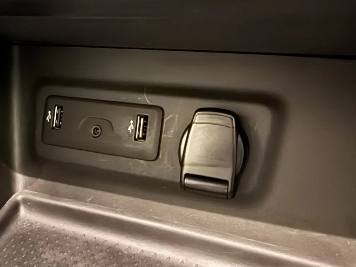 Prise USB double et prise 12V noire en gros plan dans le compartiment intérieur d'une Renault Mégane gris foncé.