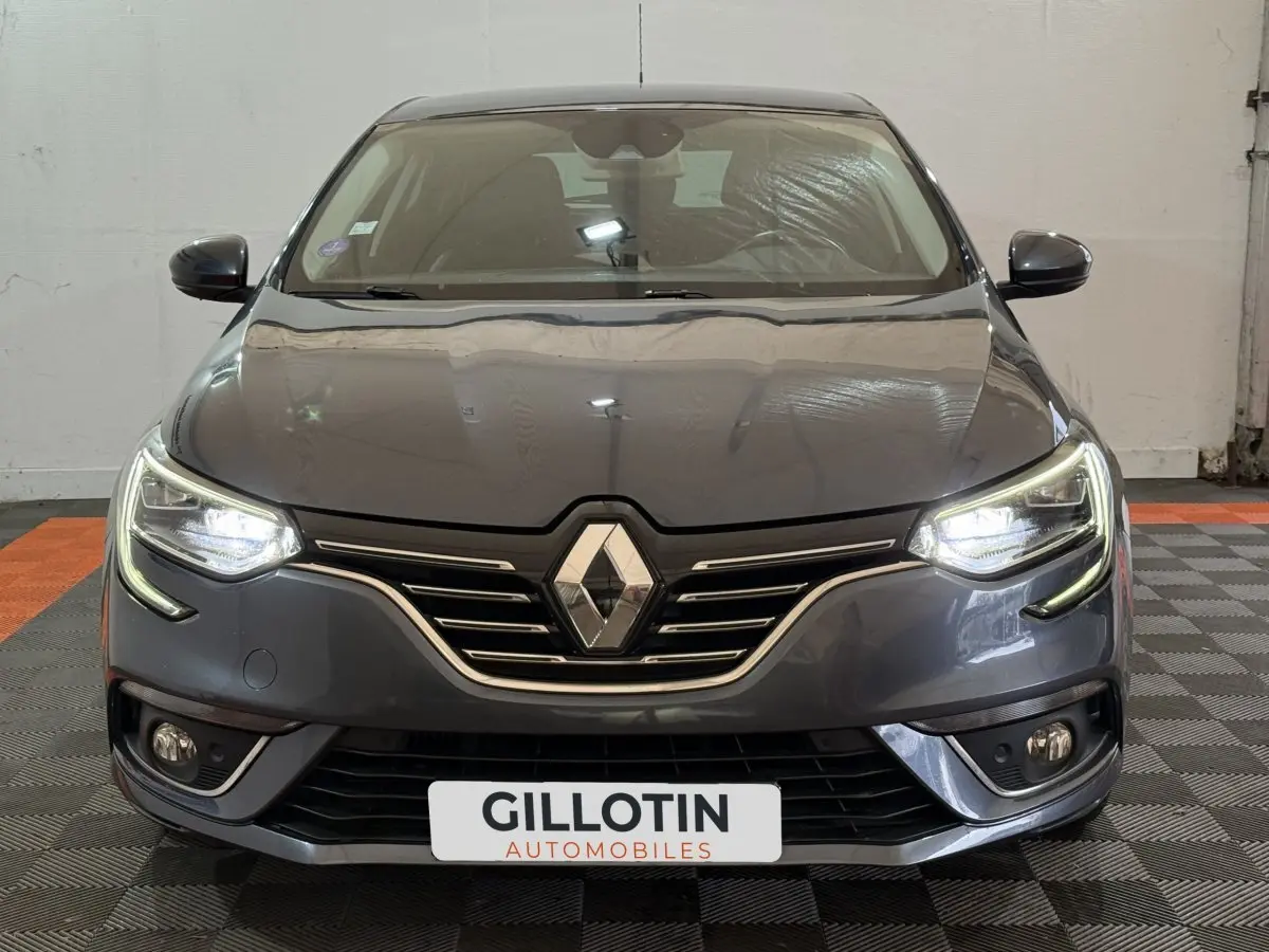 Vue frontale d'une Renault Mégane Intens gris foncé avec phares LED allumés et calandre chromée.