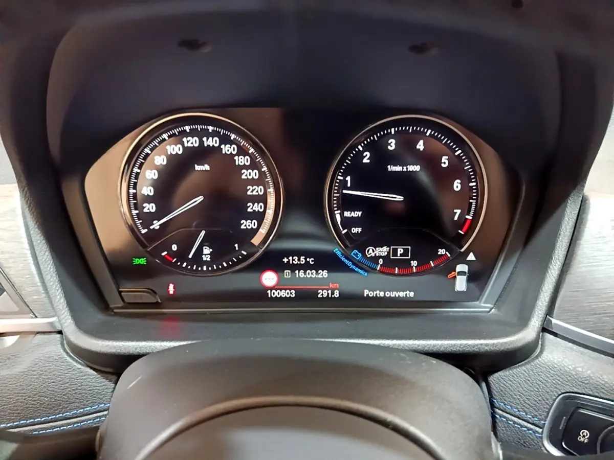 Gros plan sur le tableau de bord numérique de la BMW X2 bleu, affichant vitesse, compte-tours et informations de conduite.