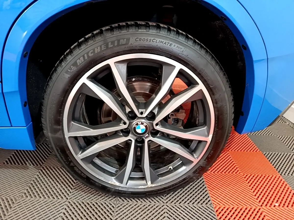Gros plan sur la roue avant droite d’un BMW X2 bleu, jante alliage à double branche en V.